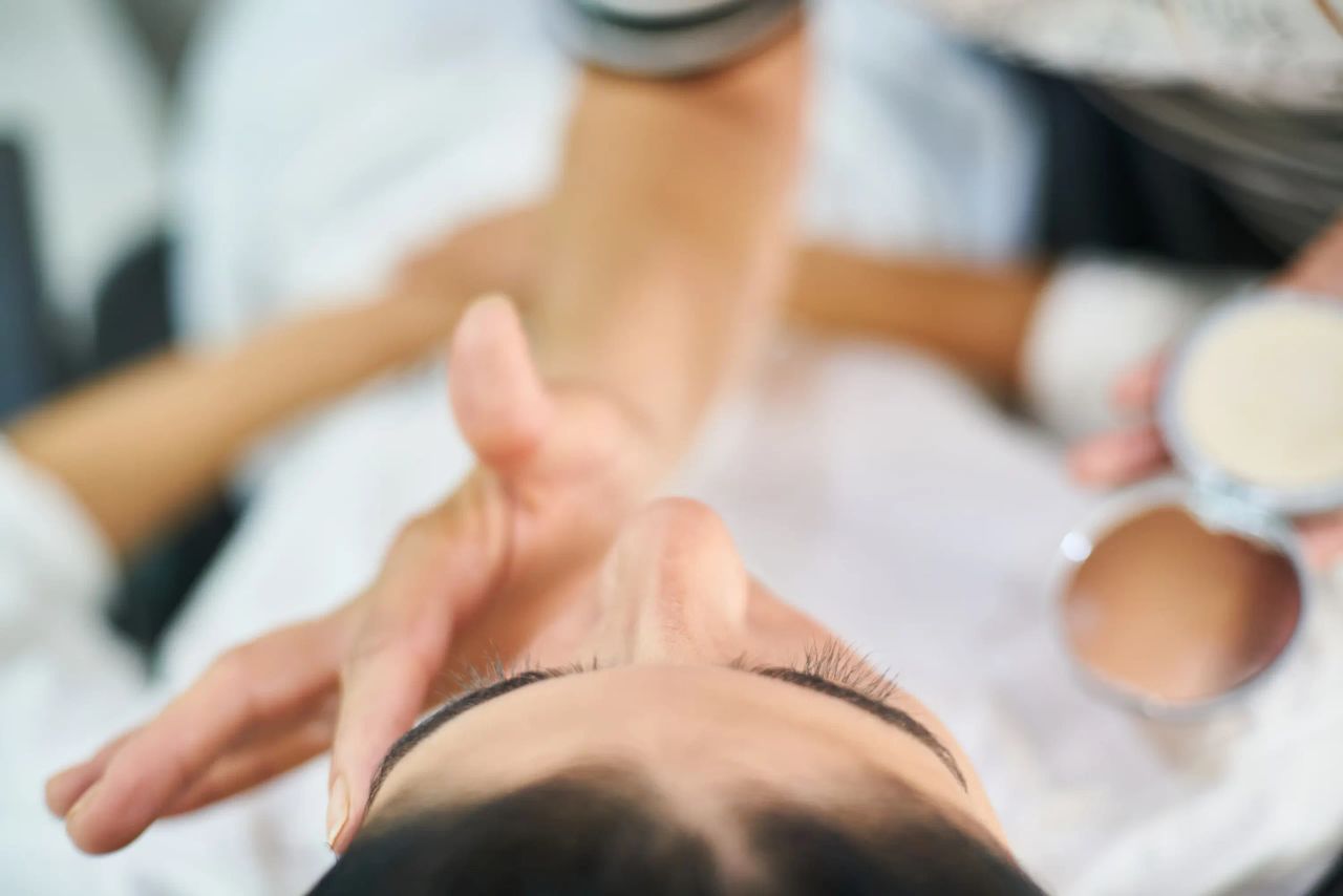 Mani dell'estetista sul viso di una cliente sdraiata sul lettino